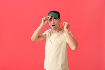 Shocked young man with sleeping mask and ear plugs on red background