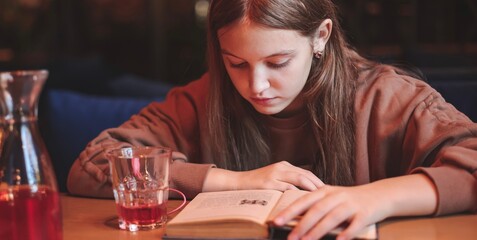 A cute teenage girl reading book in cafe. Education, leisure, hobby, back to school banner.