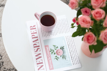 Vase with beautiful fresh roses and cup of coffee on table in room, closeup