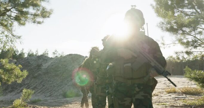 Soldiers march in line on a sandy terrain, on a training ground among trees, armed with a rifle in their hands, uniforms, helmets, defense of territory, military exercises, provocations