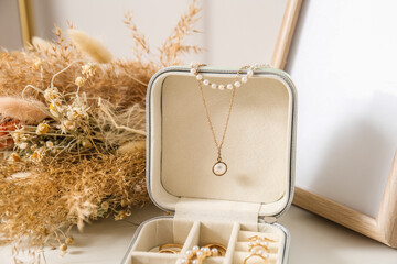 Opened box with stylish jewelry and flowers on white table