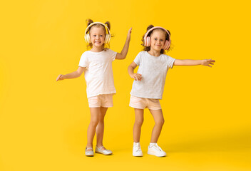Cute little girls in headphones dancing on yellow background