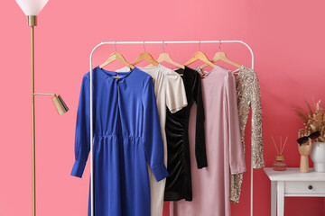 Hanger with stylish dresses, floor lamp and table near color wall in room