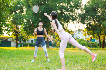 Young women playing badminton outdoors - obrazy, fototapety, plakaty