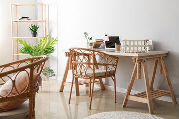 Modern workplace with laptop and wicker chair near light wall