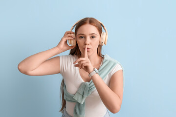 Fototapeta premium Cool young woman listening to music and showing silence gesture on color background