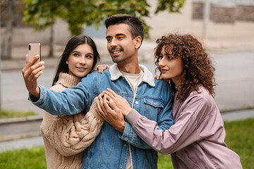 Obraz premium Man with two beautiful women taking selfie outdoors. Polyamory concept