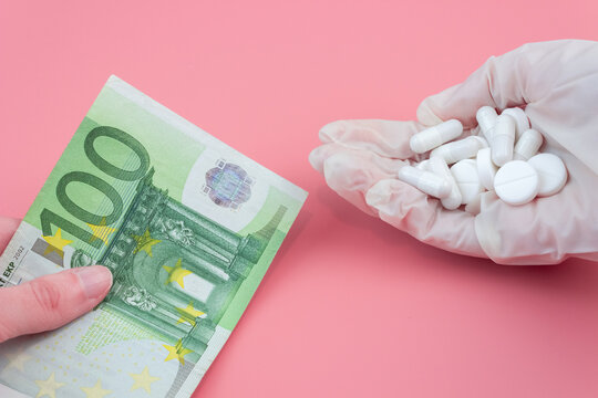 A hand gives a bill of one hundred euros towards a hand in a medical glove with a pill on a pink background. Drug shopping concept