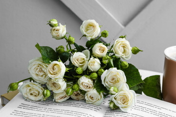 Bouquet of beautiful roses and book on table near light wall