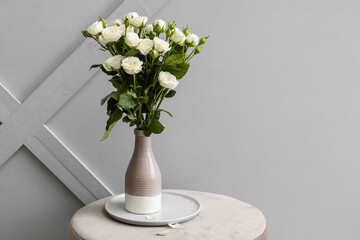 Vase with bouquet of beautiful roses on table near light wall