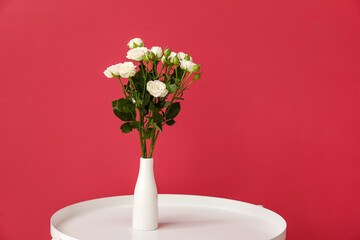 Vase with bouquet of beautiful roses on table near red wall