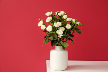 Vase with bouquet of beautiful roses on table near red wall