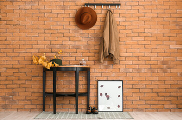 Autumn leaves with hat on table and picture frame near brick wall in hallway