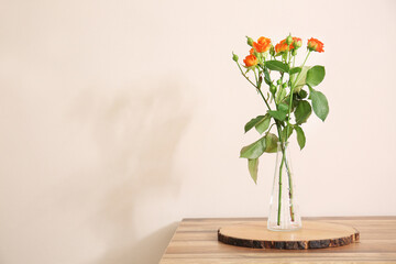 Vase with beautiful orange roses on table against light wall