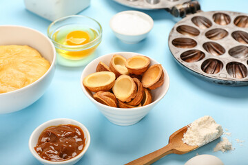 Bowls with tasty walnut shaped cookies and boiled condensed milk on blue background