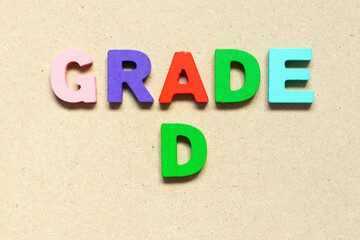 Color alphabet letter with word grade D on wood background