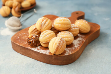 Wooden board of tasty walnut shaped cookies with boiled condensed milk and sugar powder on color background