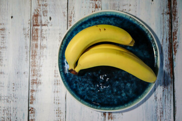 ripe yellow bananas in a beautiful glazed plate bowl on wooden table close up