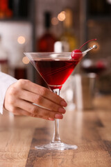 Woman with glass of tasty Manhattan cocktail on wooden table