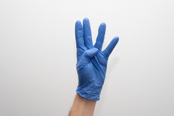 Mano con guantes azules de vinilo sobre fondo blanco, haciendo el gesto número cuatro con los dedos, indicando numero 4 con los dedos. - obrazy, fototapety, plakaty
