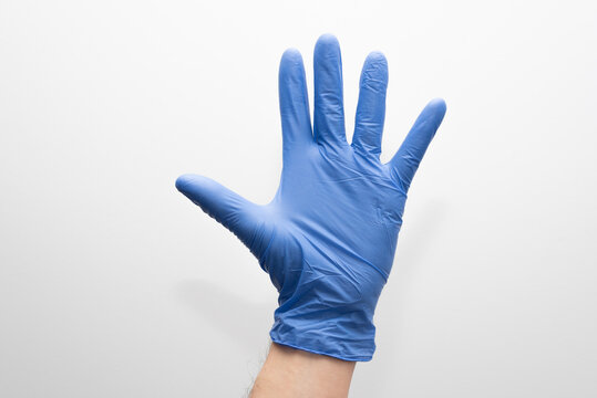 Una mano  de hombre con guantes azules de latex con la palma abierta sobre fondo blando.
