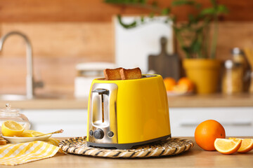 Yellow toaster with bread and orange slices on table in kitchen