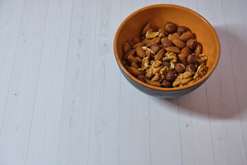 brown clay bowl with nuts: walnuts, almonds and hazelnuts on a light background