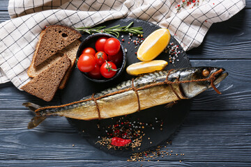 Board with smoked mackerel fish and bread on black wooden background