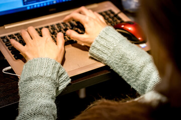 Fototapeta premium A young white woman in a light blue sweater is sitting at her workplace at the office her back to the camera and working on a golden laptop computer with her hands on the keyboard