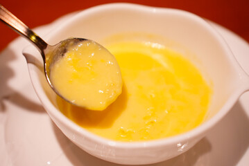 A stylish small white bowl of sweet corn soup made of brand corn from Hokkaido Japan with a round metal spoon and a white plate underneath