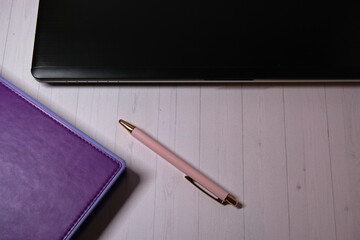 purple notepad, black laptop and pink pen on a light wooden table