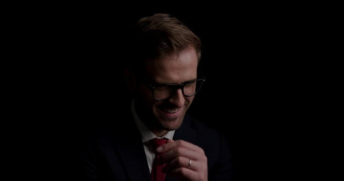young handsome businessman scratching his chin, wearing eyeglasses and looking away on dark background