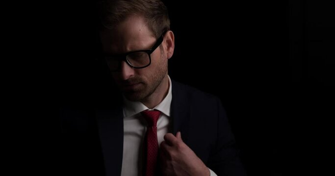 sexy businessman looking down, arranging his suit, wearing eyeglasses and looking at the camera