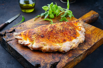 Traditional Italian pizza calzone with tuna fish and onions served as close-up on a rustic old wooden board