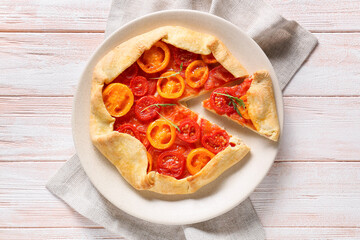 Plate with tasty tomato galette on light wooden background