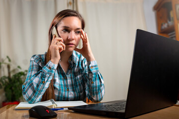 Mujer preocupada hablando por telefno mientras trabaja con su laptop