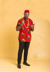 Igbo Traditionally Dressed Business Man Standing with Phone in Hand Looking