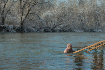 A man bathes in an icy river in the winter season. The concept of a healthy active lifestyle and hardening in cold water