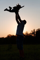 Silhouette of happy father and daughter. Smiling little girl in daddy arms at sunset.