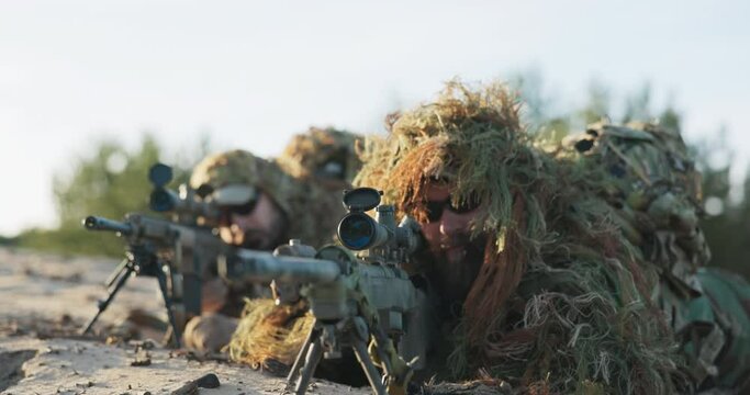 Military men in moro uniforms dressed in ghillie camouflage grass moss men lie on ground, guns on stand with scope prepare to fire on attacker from concealment training ground territorial defense