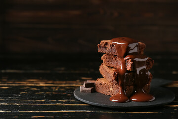 Board with pieces of tasty chocolate brownie on black wooden background