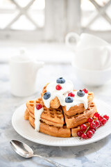 Waffles with blueberries, red currants, poured with yogurt on a white porcelain plate on the windowsill