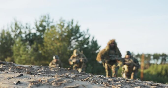Military men in moro uniforms wearing ghillie grass moss camouflage run and lie down on ground guns on stand with scopes prepare to fire at attacker from concealment training ground