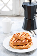Waffles with yogurt on a white porcelain plate with black geyser coffee maker on the windowsill