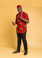 Igbo Traditionally Dressed Business Man Standing with Phone in Hand and smiling