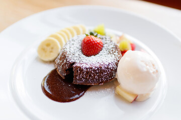 Chocolate lava cake with vanilla ice cream and banana in a white plate on blurred restaurant background.