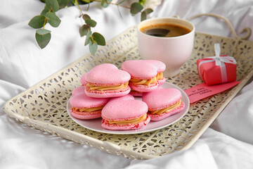 Plate with tasty heart-shaped macaroons on bed