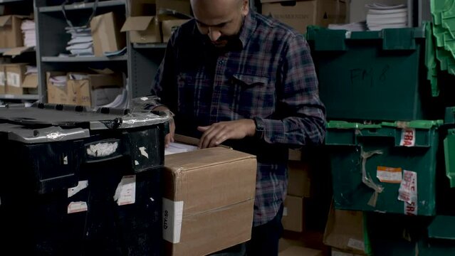 A close up shot of a handsome male office employee returning to continue his search through a box of old archived documents in a cluttered storeroom