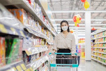 Beautiful attractive asian woman wearing medical face mask and rubber gloves for protected virus and bacteria smile with shopping cart in supermarket happiness and enjoy,Shopping in Grocery Concept
