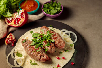 Three kebabs on thin pita bread, with herbs, onions and pomegranate seeds. Spicy tomato sauce, herbs and pomegranate in the background.